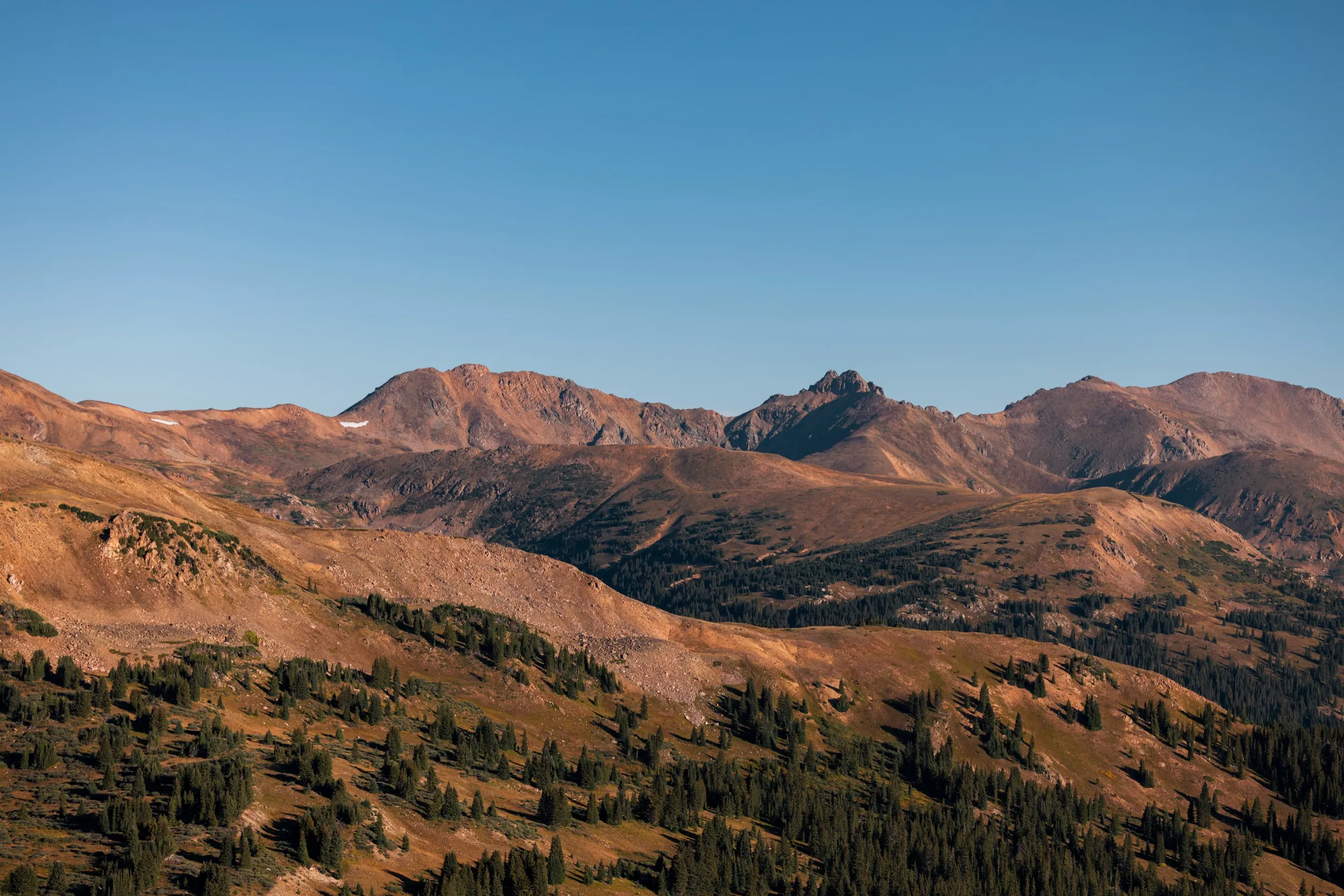 Wide view of golden alpine ridges and a rocky peak under a clear sky
