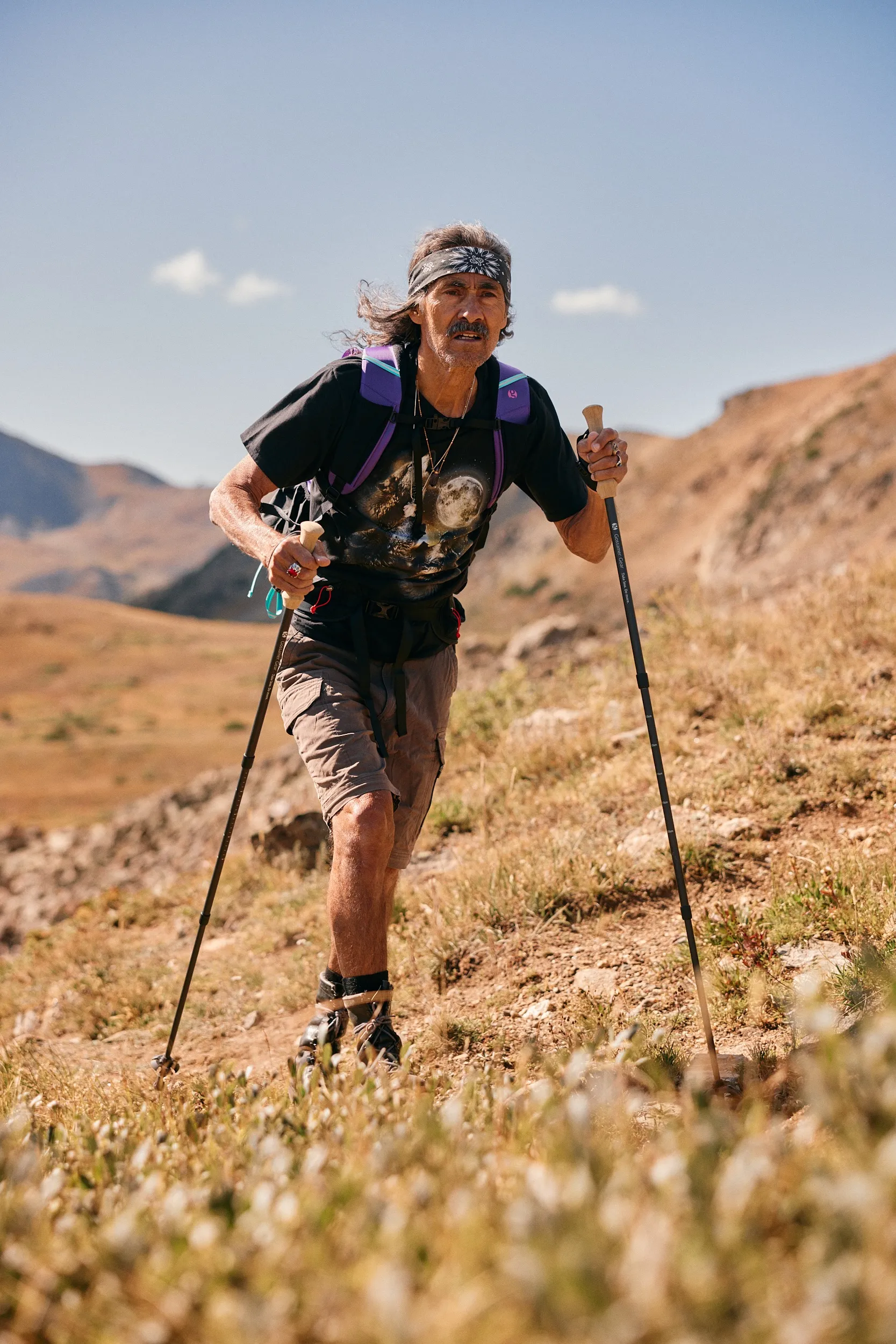 Hiker with a purple pack and trekking poles climbing a grassy slope