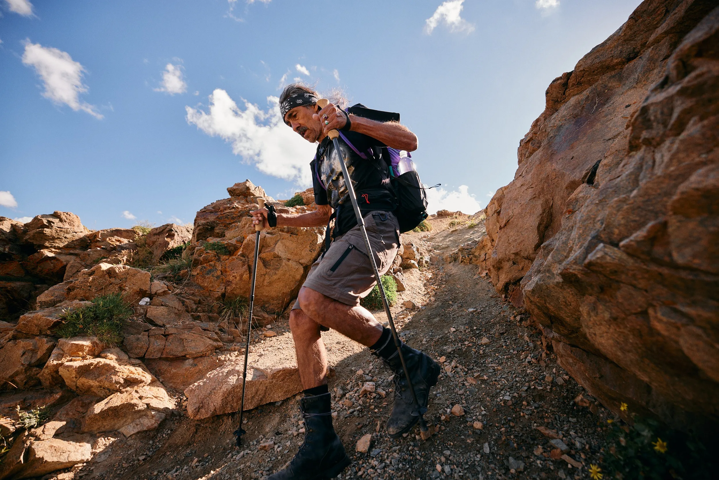 Hiker with trekking poles stepping up a rocky trail between boulders