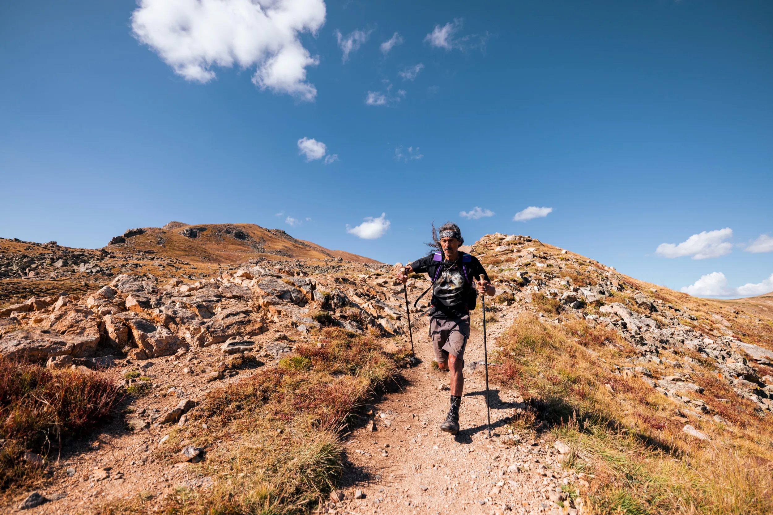 Hiker walking toward the camera on a rocky trail above treeline